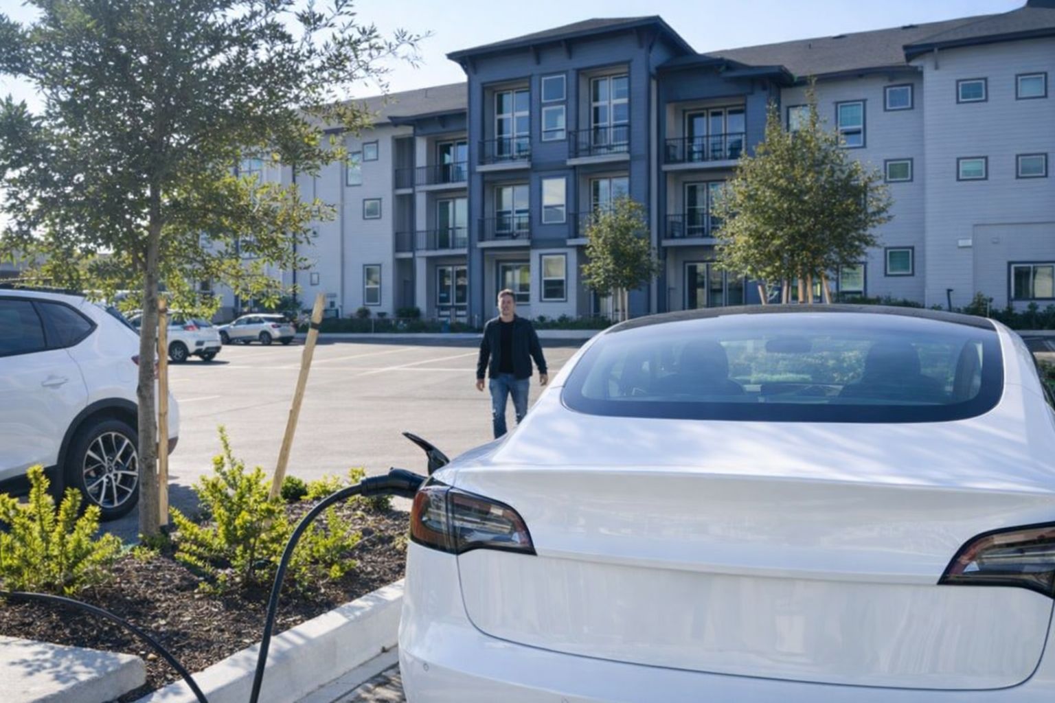 Valkoinen sähköauto latauksessa kerrostalon parkkipaikalla.