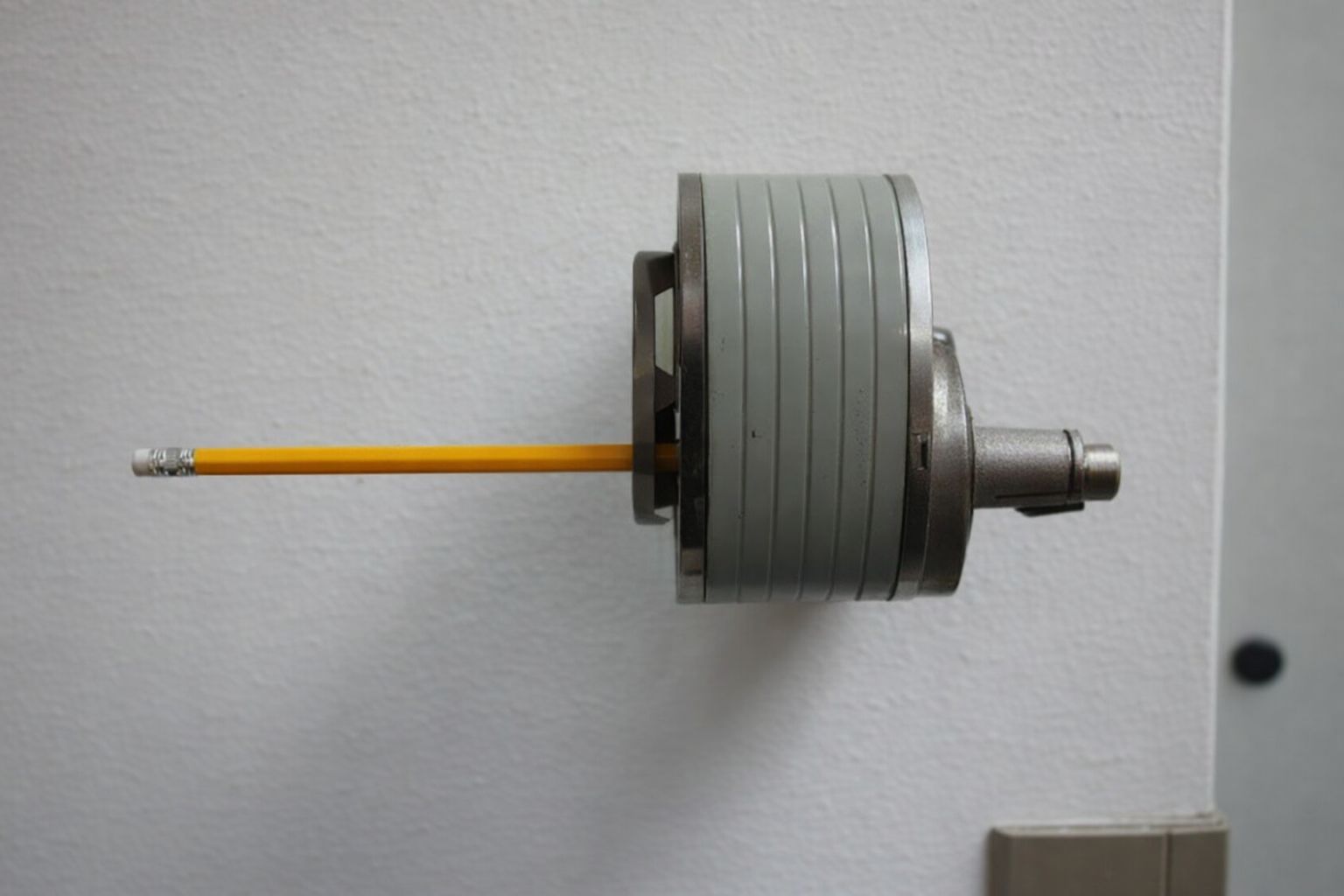 Keltainen lyijykynä työnnettynä pyöreän metallisen teknisen laitteen läpi.